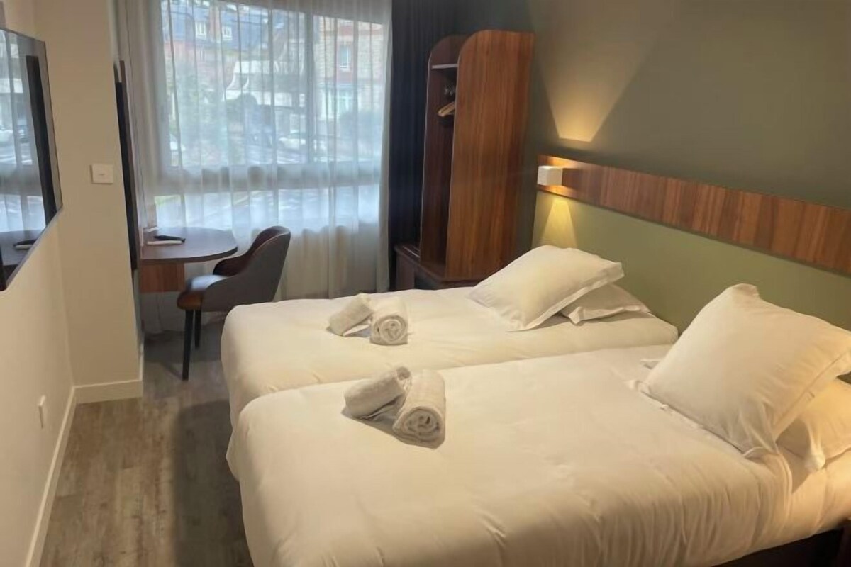 Une chambre d’hôtel avec deux lits, un bureau, une chaise et une armoire.