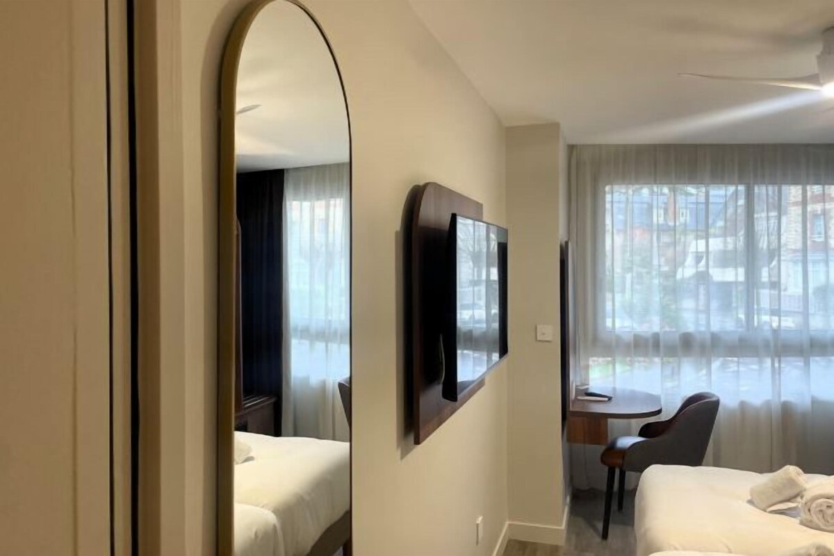 A hotel room with a bed, a desk, a chair, a television, and a large mirror.