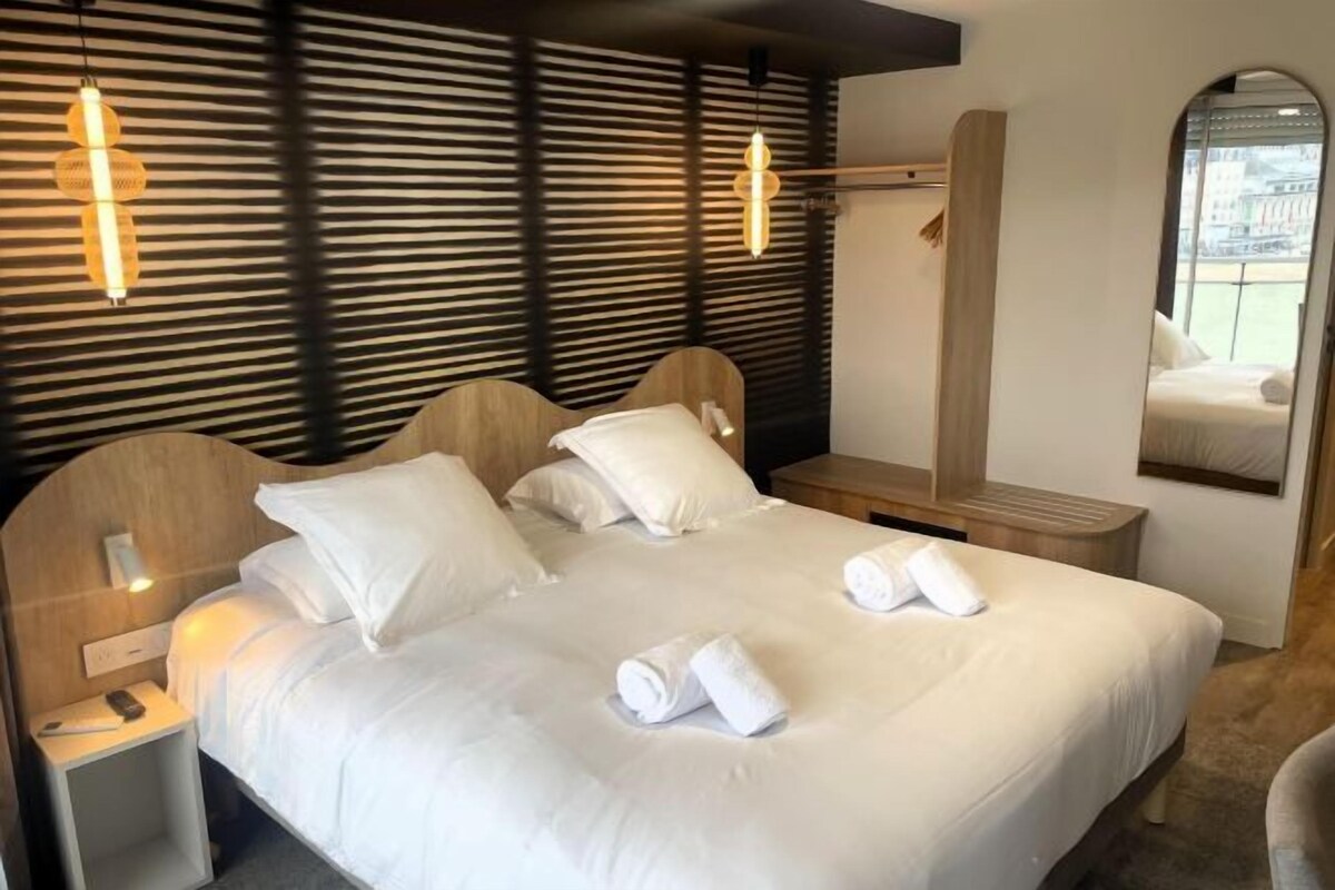 A hotel room with a bed, bedside tables, a mirror, and a window.