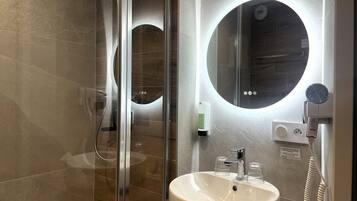 A modern bathroom with a glass shower enclosure, a round mirror, a white sink, and a handheld showerhead.