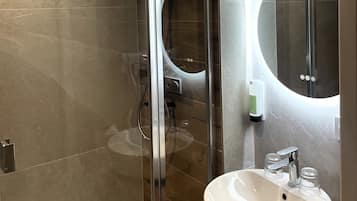 A modern bathroom with a glass shower enclosure, a round mirror, and a white sink with chrome fixtures.