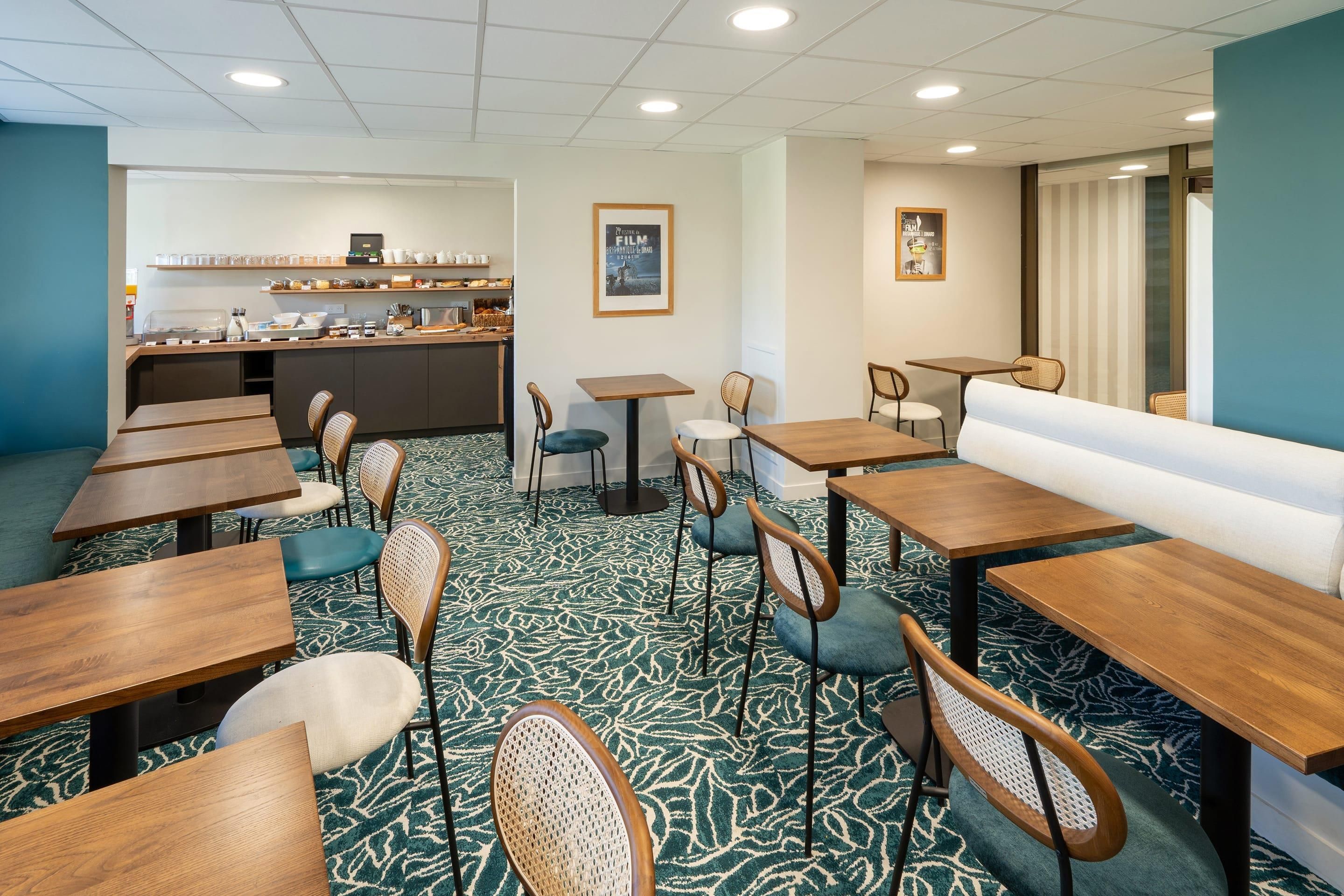 A hotel dining area with multiple tables and chairs, a counter with food and drink options, and a patterned carpet.