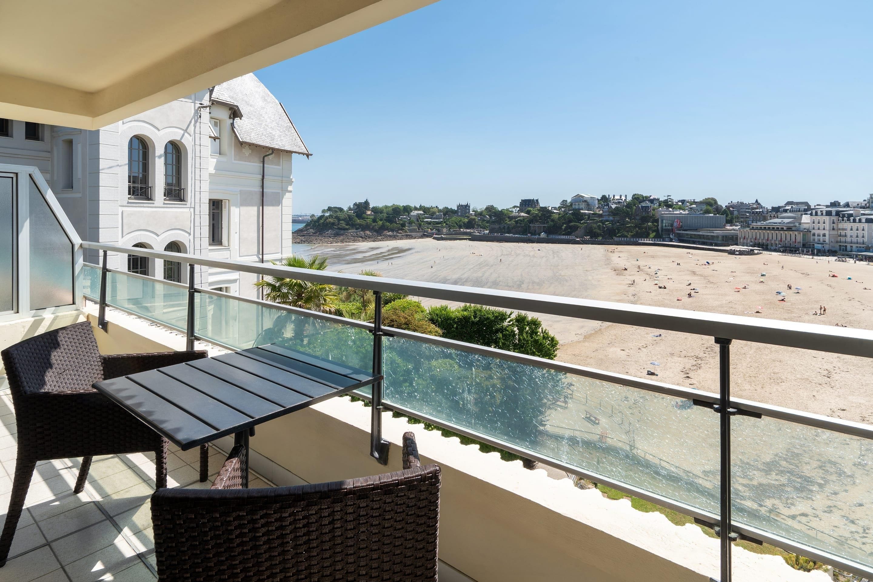 A balcony with a view of a beach and a building with arched windows.