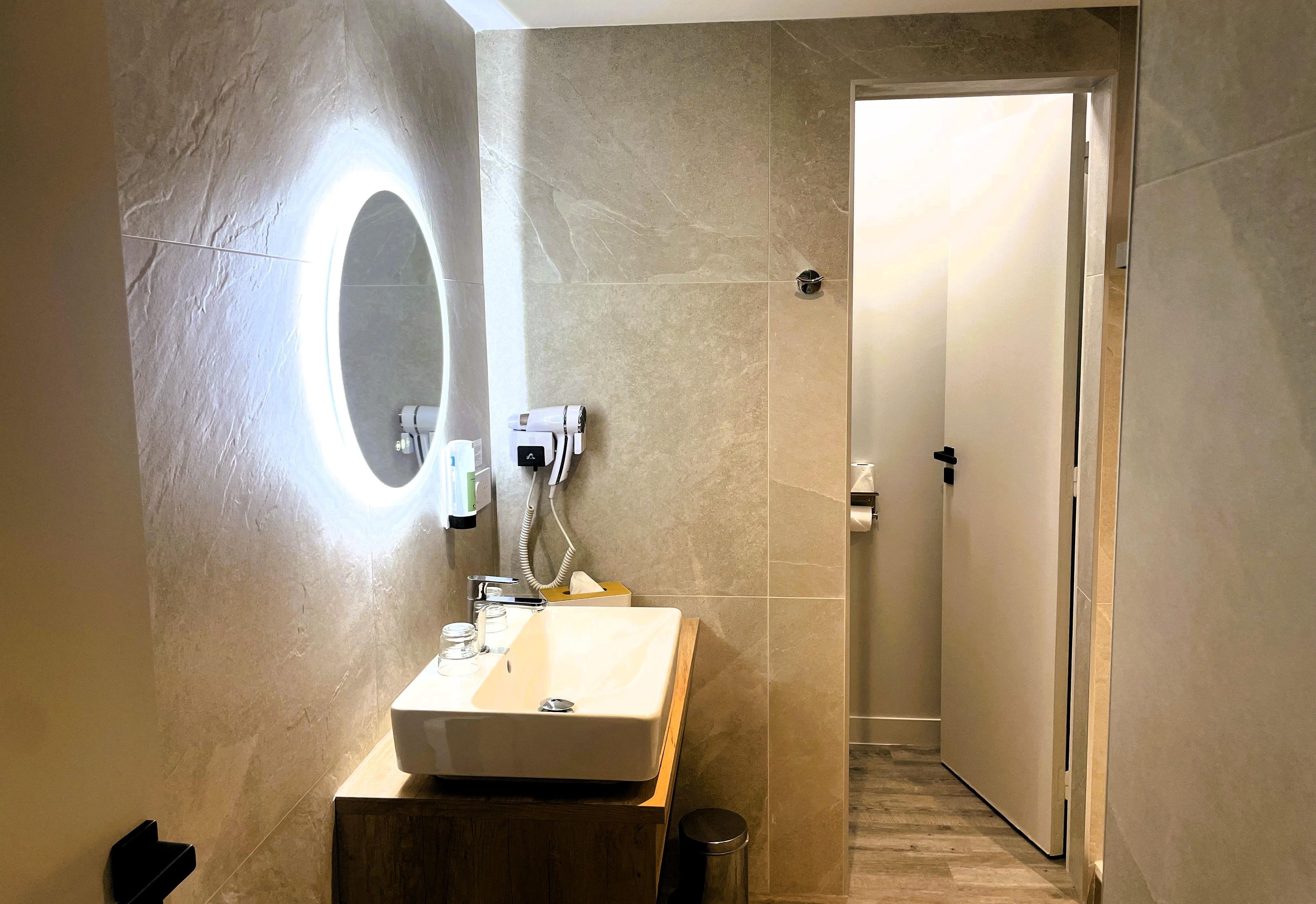 A bathroom with a vanity, mirror, and towel dispenser.