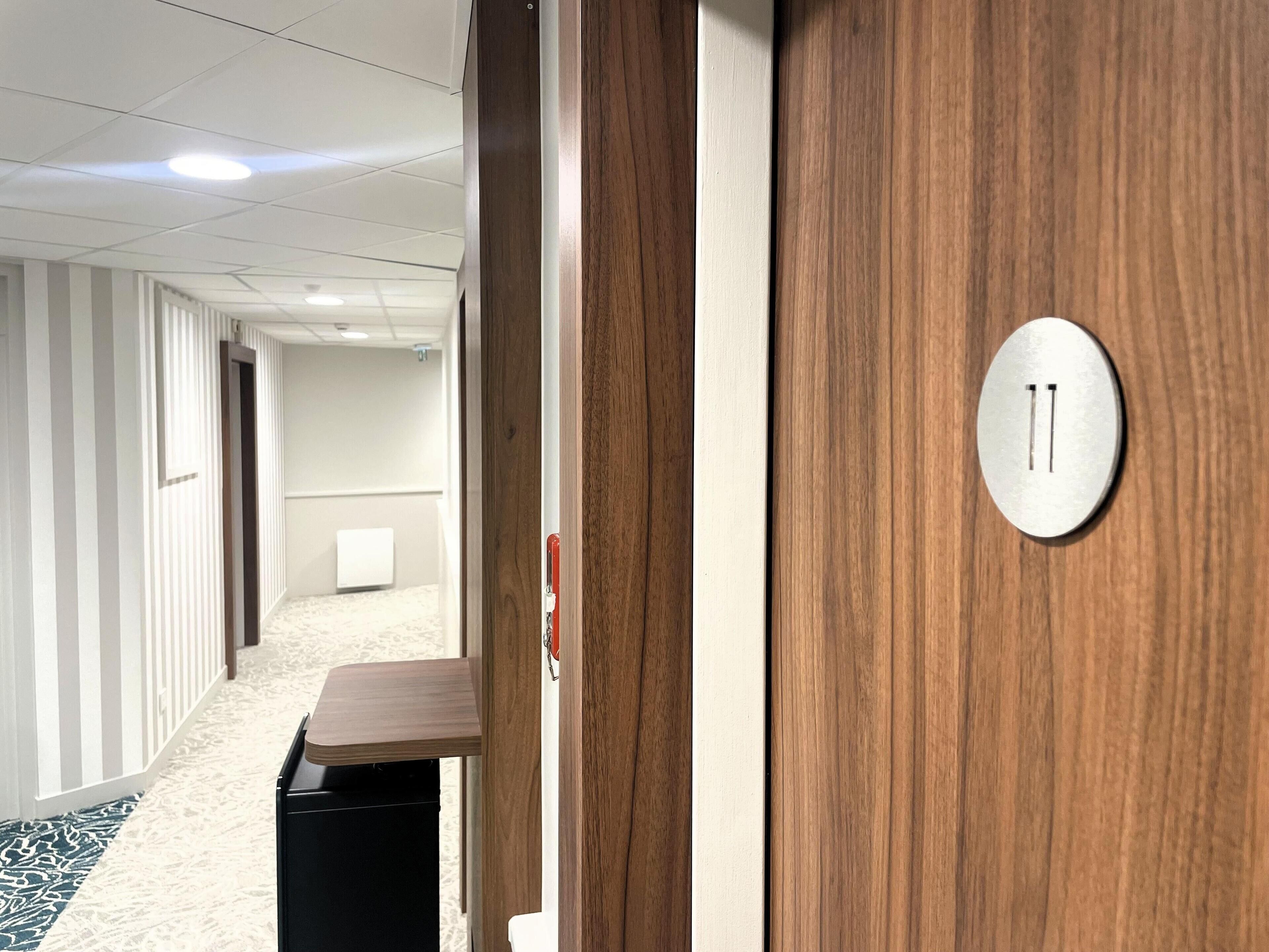 A hallway with a wooden door, a white wall, and a carpeted floor.