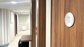 A hallway with a wooden door, a white wall, and a carpeted floor.