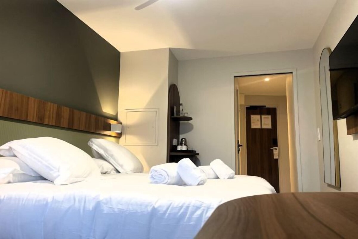 A hotel room with a bed, a bedside table, a mirror, and a door leading to another room.