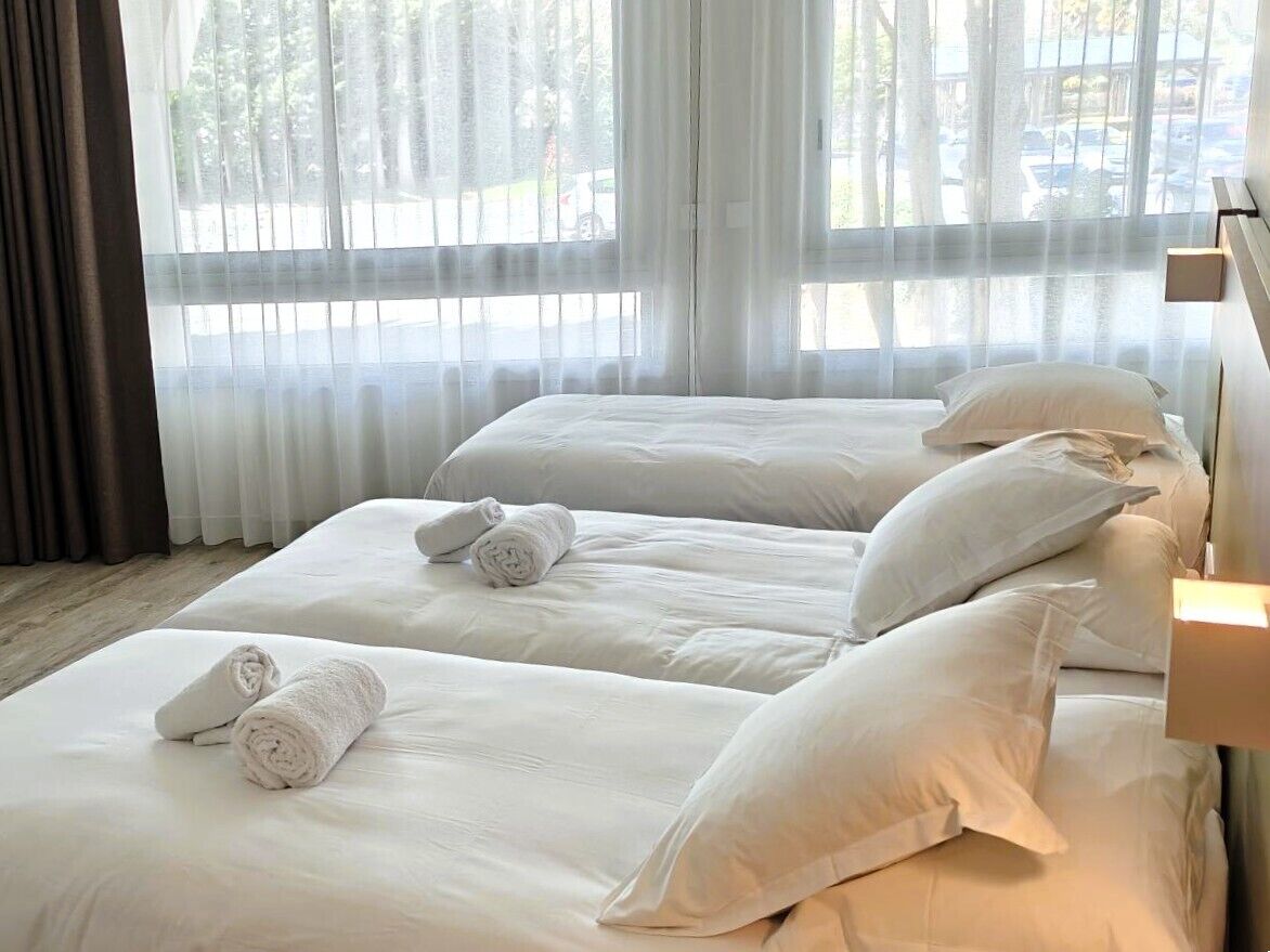 Une chambre d’hôtel avec deux lits, du linge de lit blanc et une vue à travers des rideaux transparents.