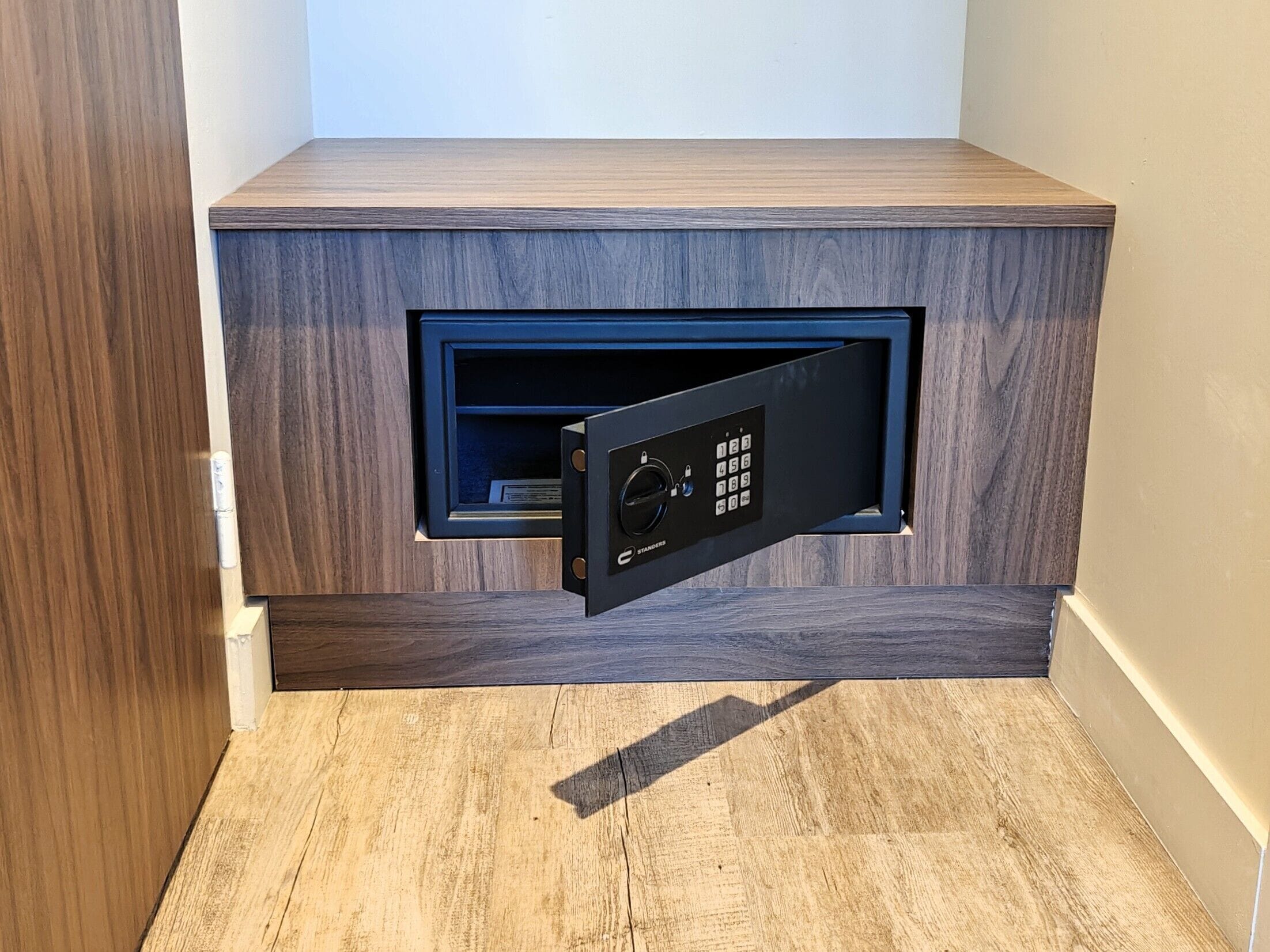 Una caja fuerte empotrada con teclado, un armario de madera y un interruptor de luz.