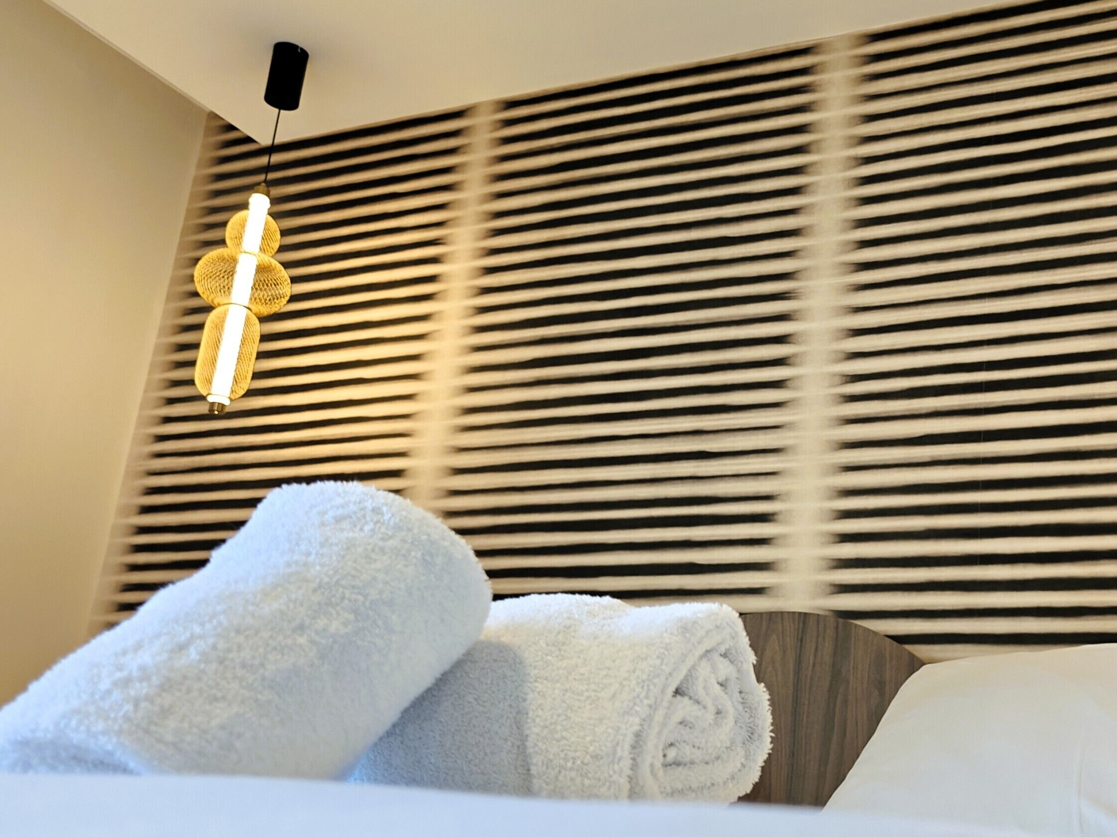 Una habitación de hotel con cama, pared de listones horizontales y lámpara colgante.