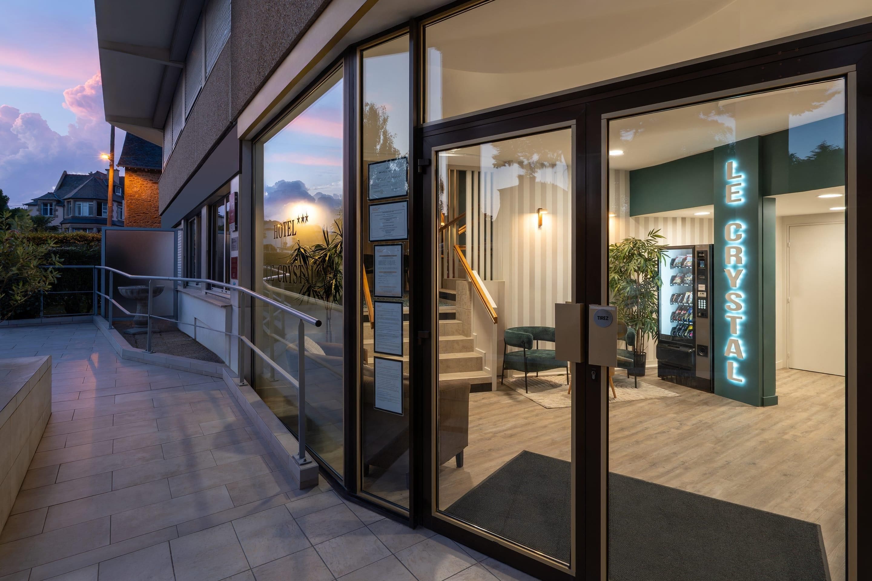L’entrée d’un hôtel avec une façade en verre, un escalier menant à l’intérieur et une enseigne indiquant « Le Crystal ».