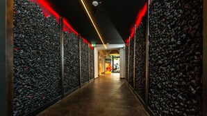 Un couloir avec un mur à texture sur un côté et un plancher poli, qui mène à un espace bien éclairé.