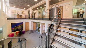 Un intérieur moderne avec un escalier, un grand téléviseur à écran plat et un coin salon agrémenté de tabourets colorés.
