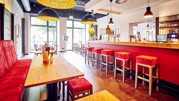 Un restaurant moderne avec des tables en bois, des sièges rembourrés de couleur rouge et des luminaires suspendus.