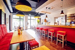 Un restaurant moderne avec des tables en bois, des sièges rembourrés de couleur rouge et des luminaires suspendus.