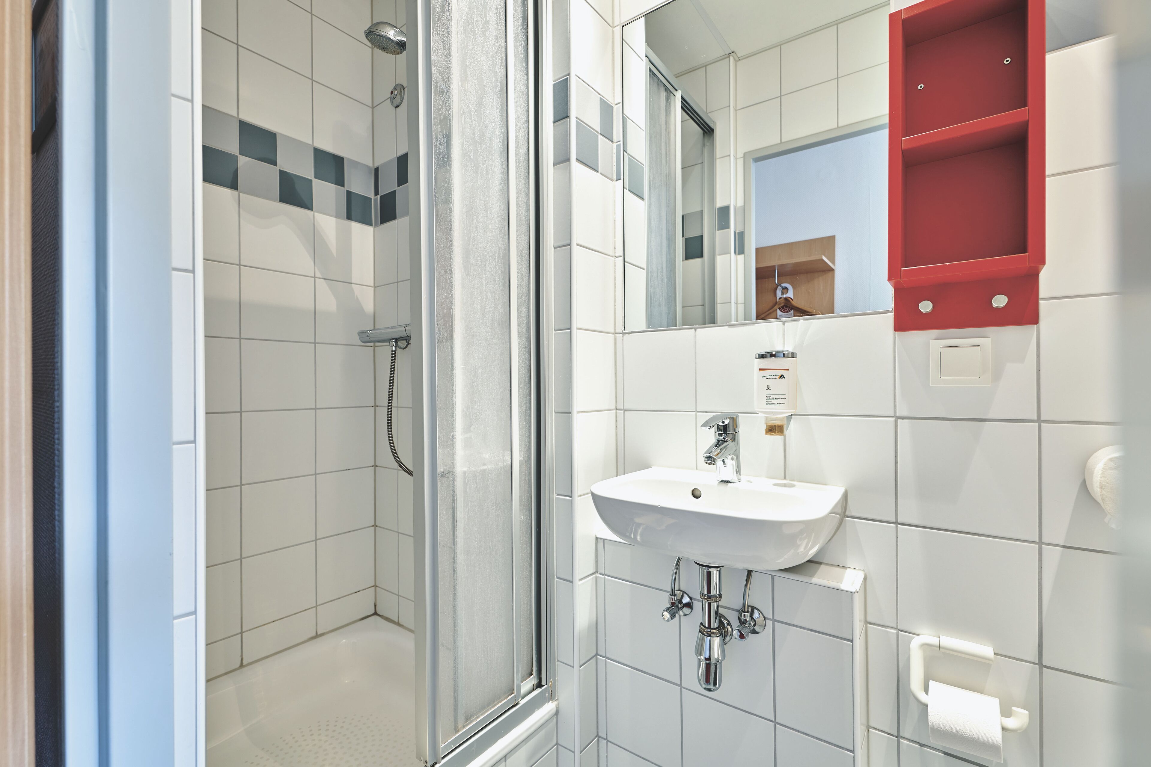 Un baño moderno con cabina de ducha de vidrio, un lavamanos blanco y un armario de medicinas rojo.