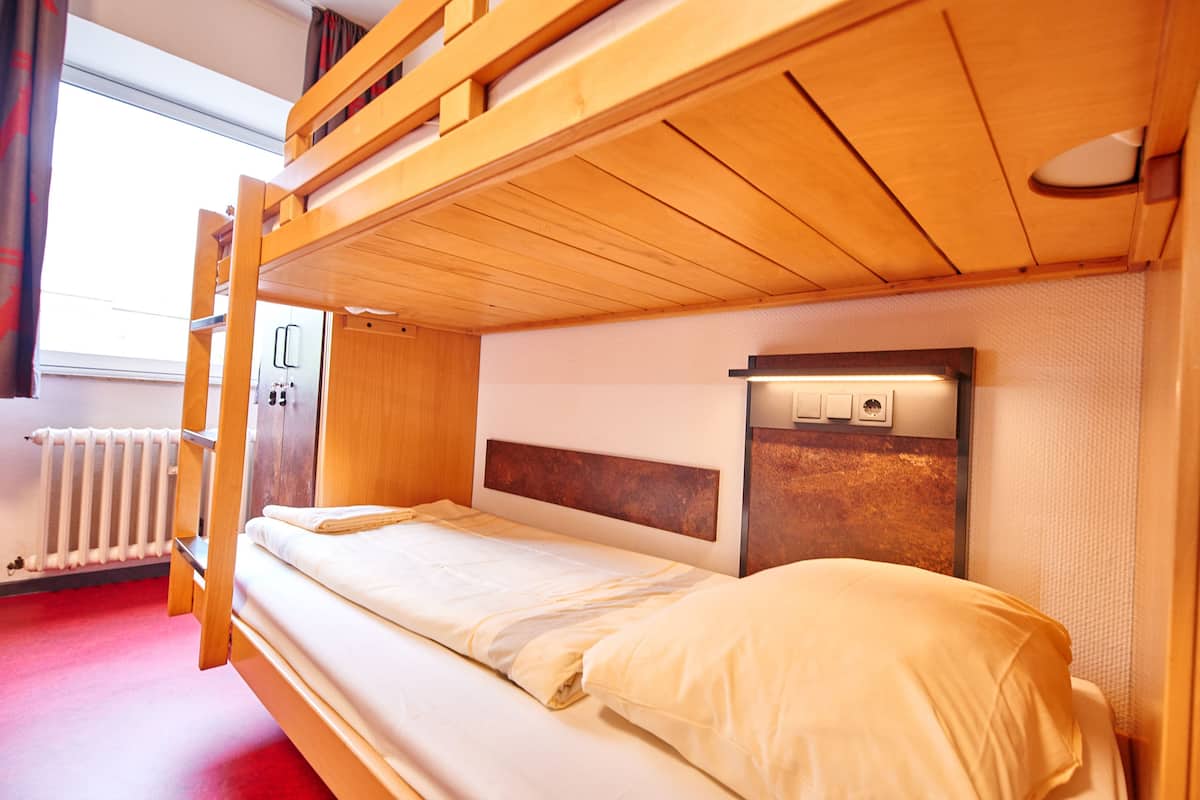 Une chambre avec un lit superposé, une tête de lit en bois, une table de chevet et une fenêtre avec des rideaux.