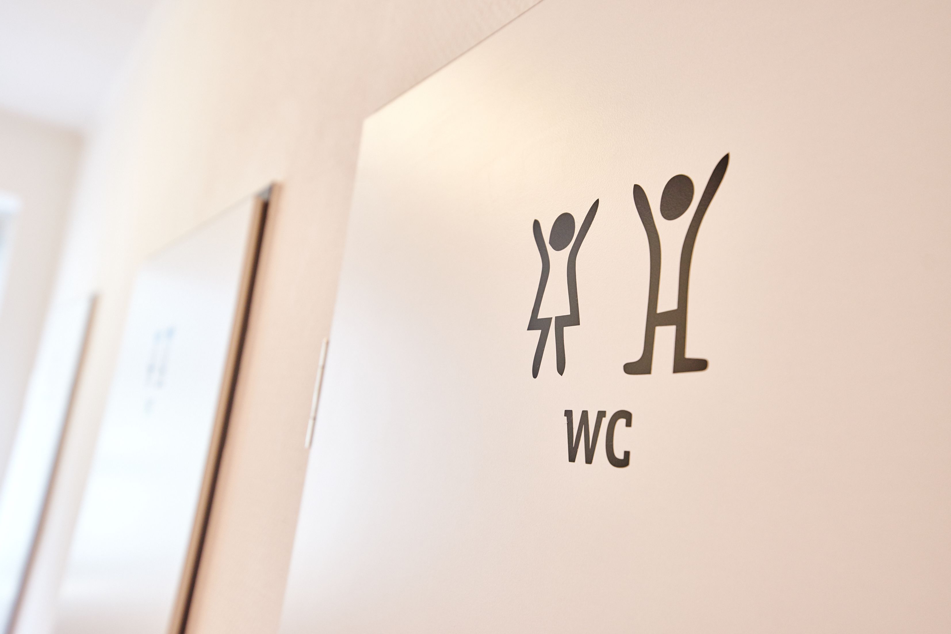 A wall with a restroom sign featuring stick figures and the letters "WC".