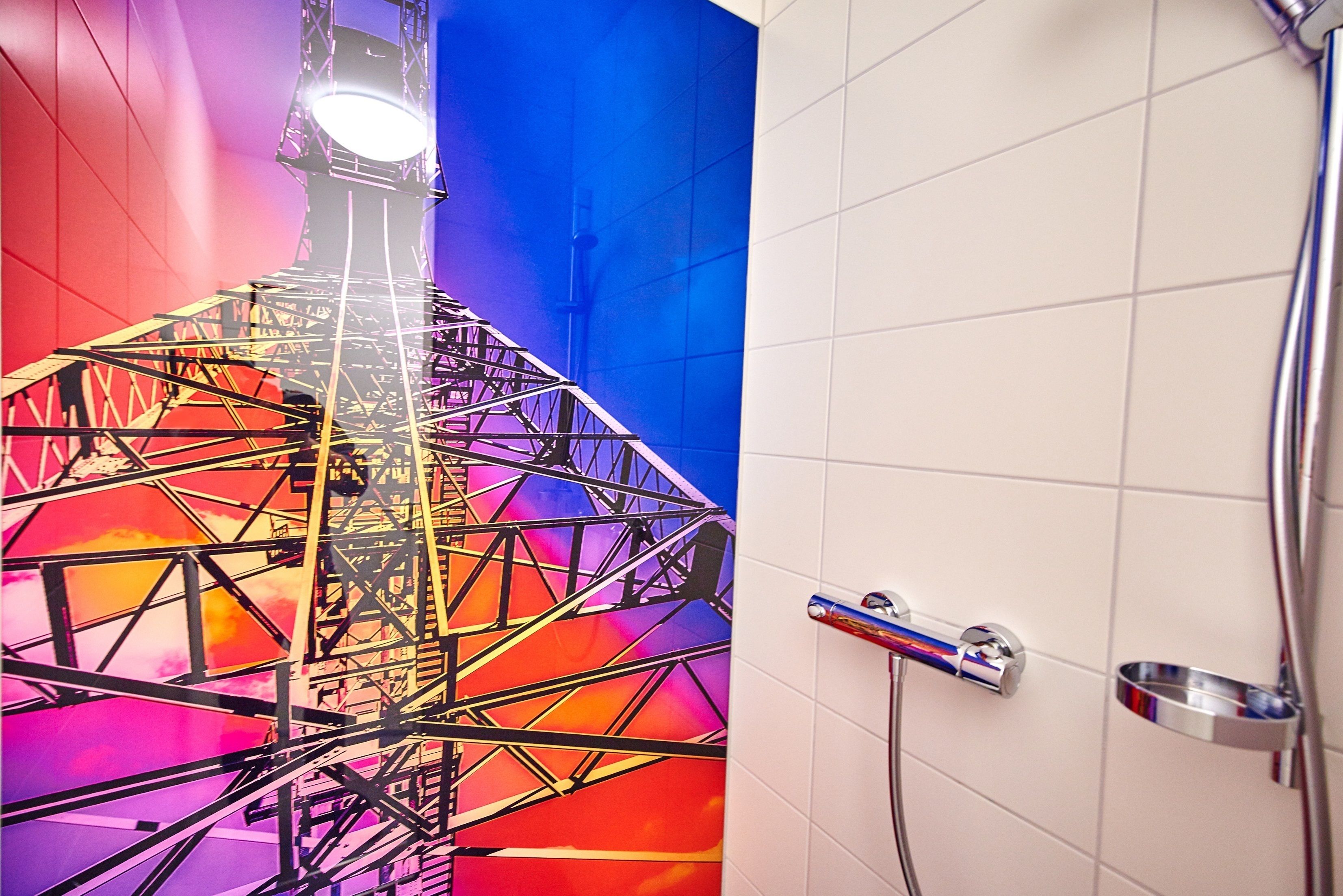 Une salle de bain ornée d’une fresque colorée représentant une grande roue, avec un espace douche et un lavabo en métal.