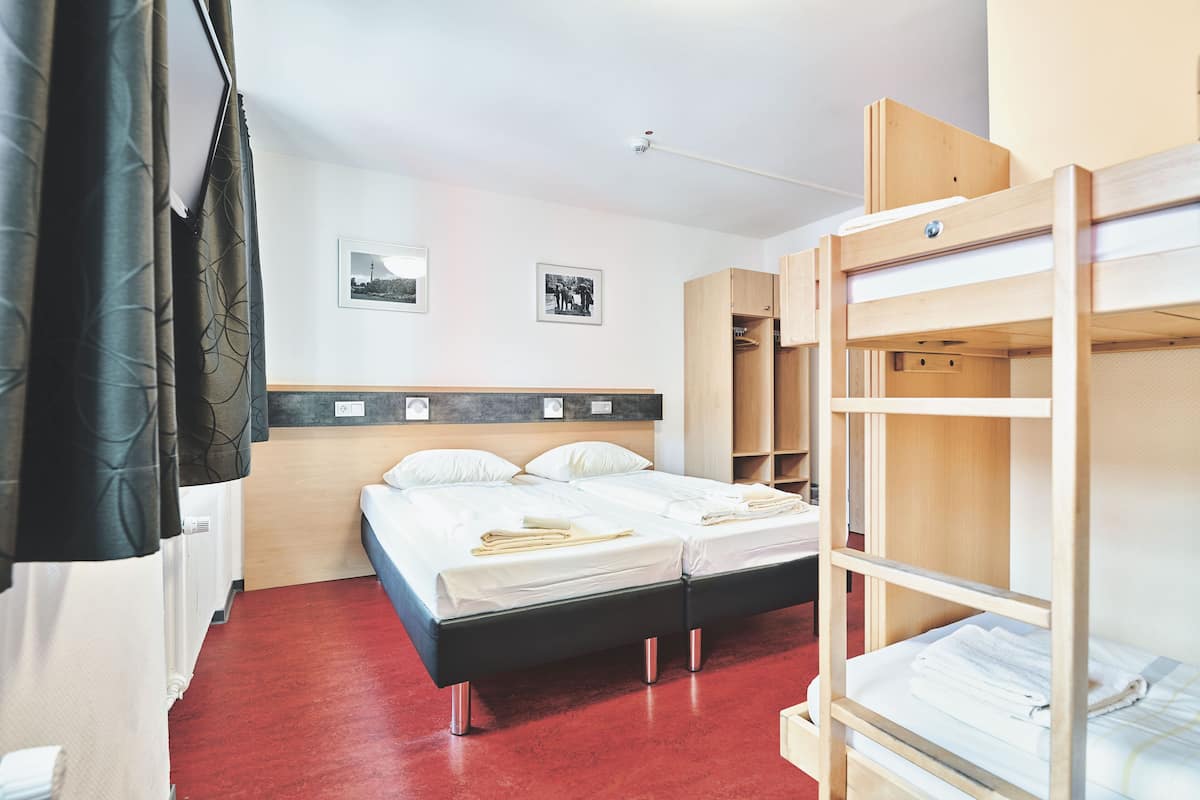 Une chambre d’hôtel avec un lit superposé, une armoire en bois, une table de chevet et deux tableaux encadrés au mur.
