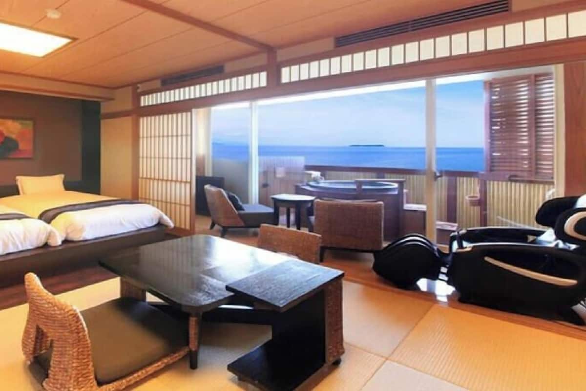 Ein Hotelzimmer mit Bett, einem kleinen Tisch, Stühlen und Meerblick.