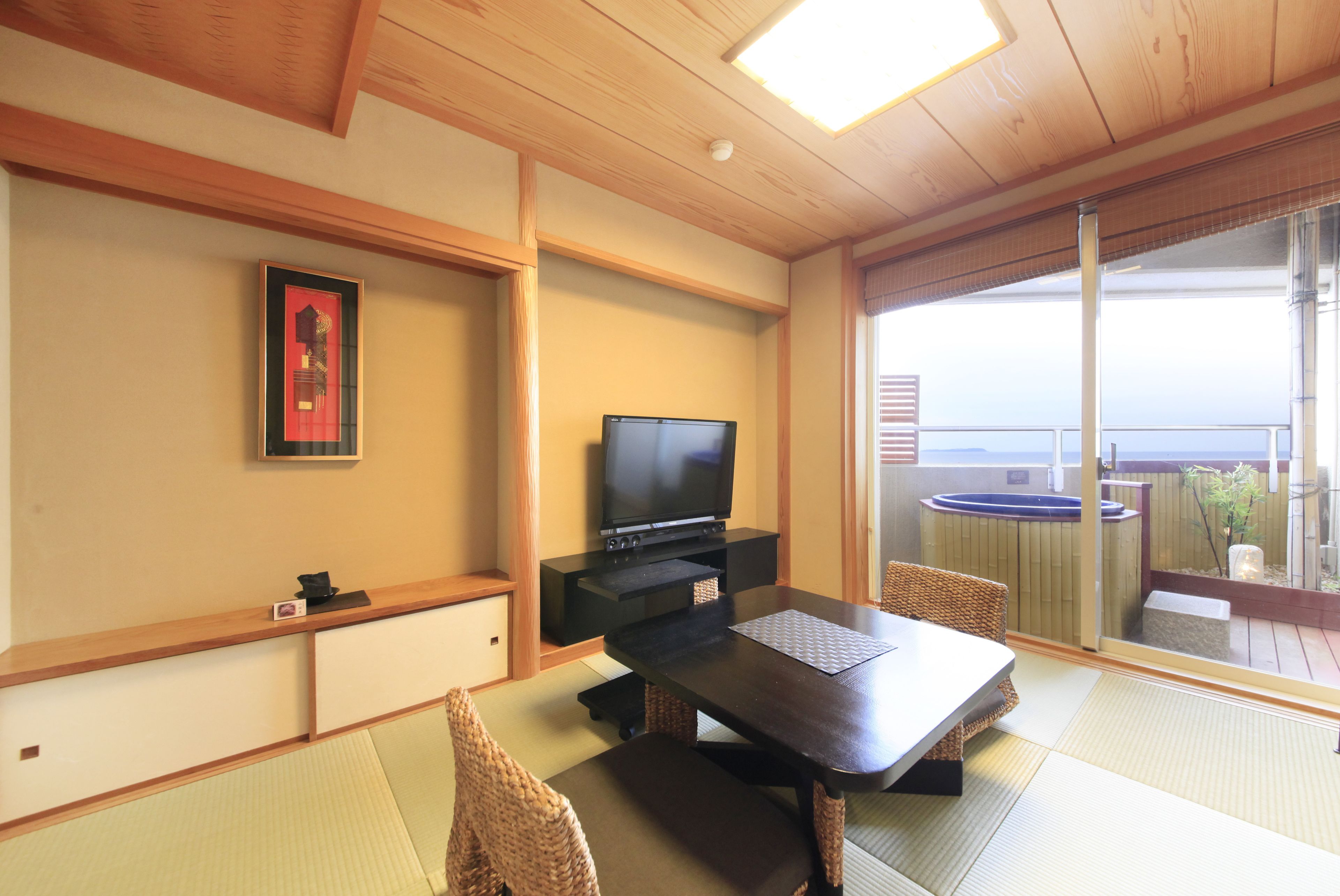 Una habitación con suelo de tatami, televisión, una mesa de comedor y vistas al mar a través de amplios ventanales.