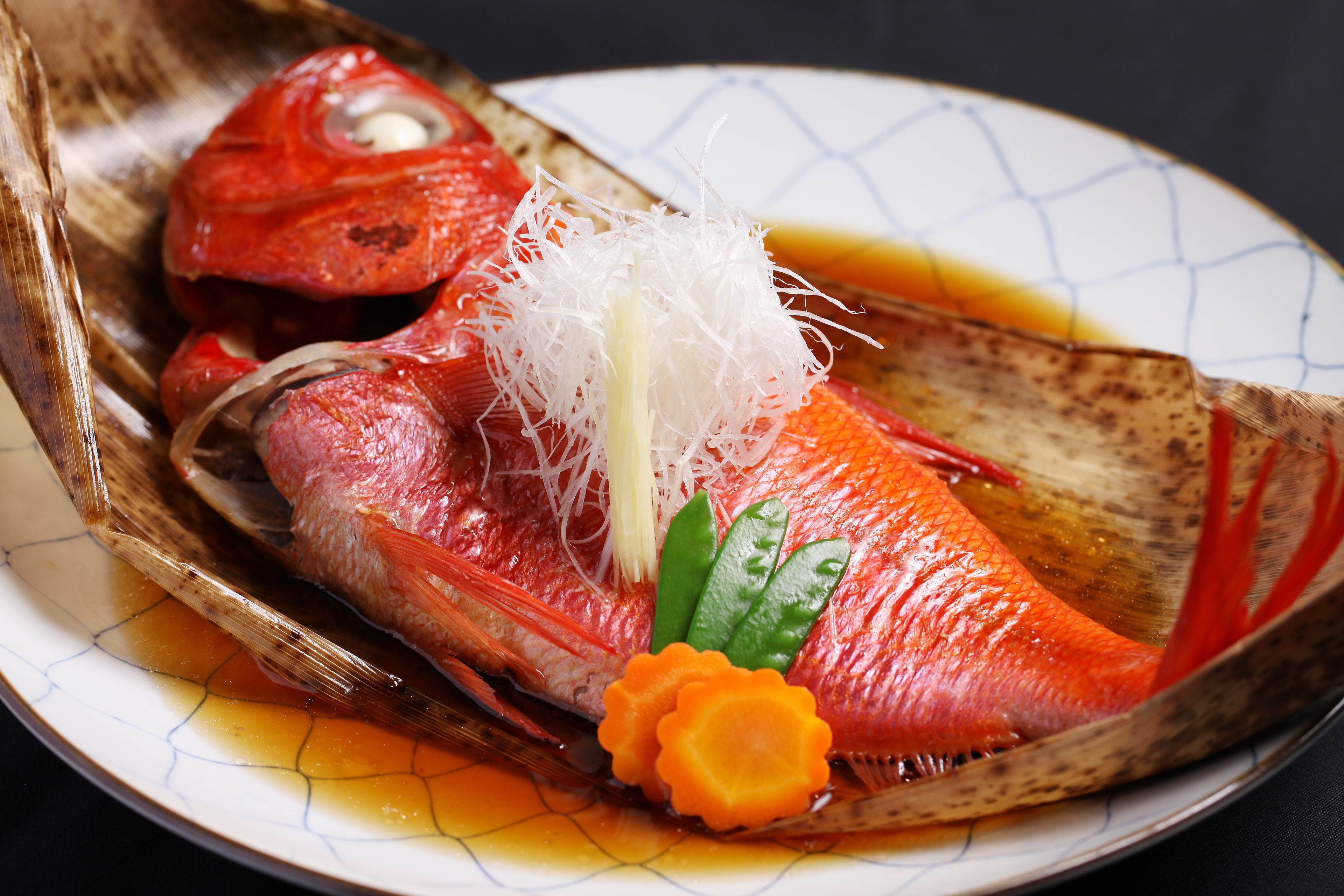 A dish of raw fish with garnish, served on a plate with a patterned rim.