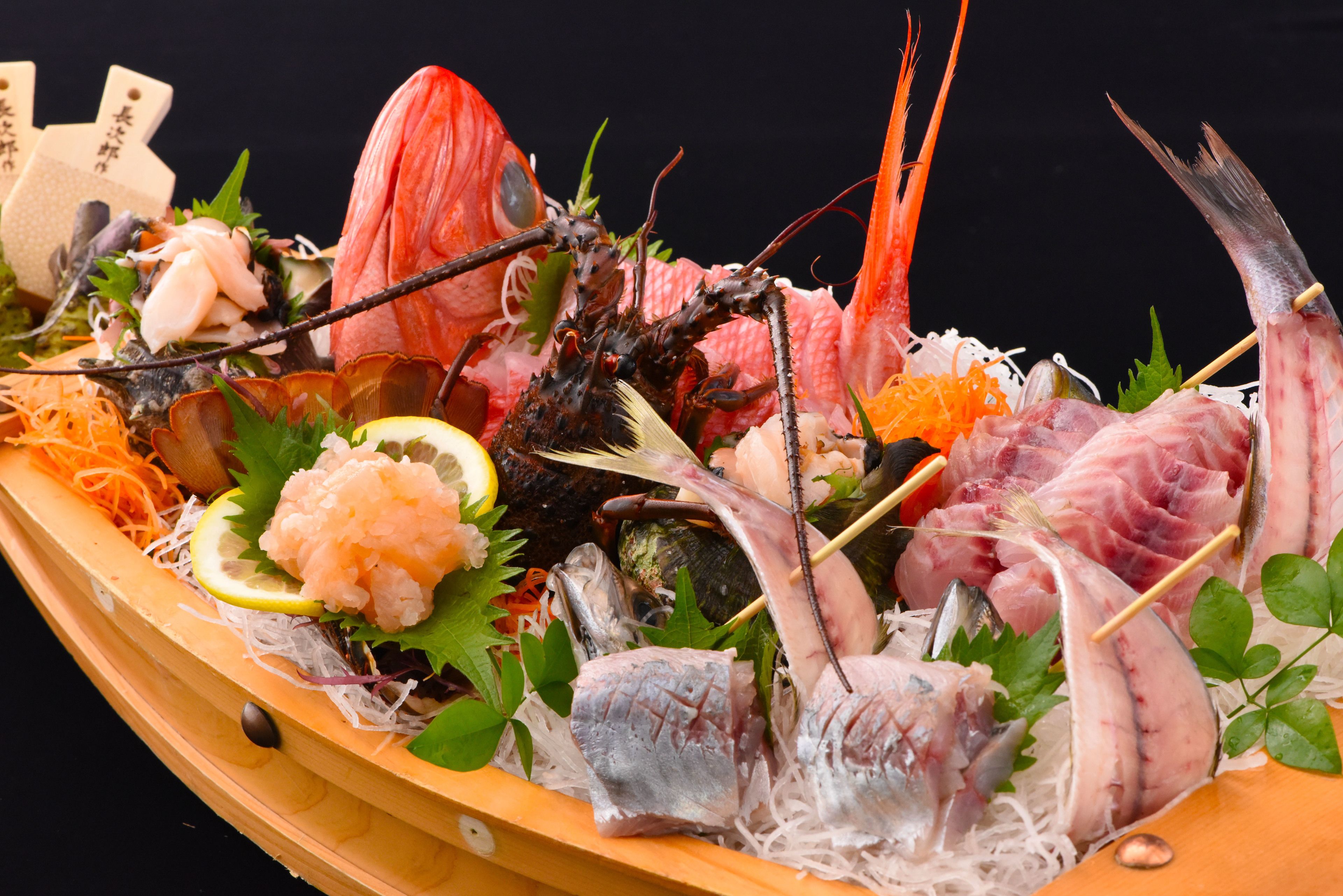 A wooden boat filled with various seafood items, including shrimp, fish, and other seafood, displayed on a bed of shredded seaweed and garnished with lemon slices and green leaves.