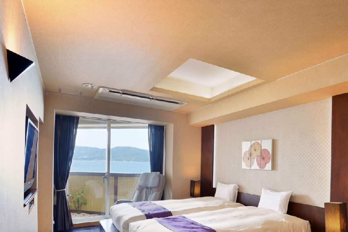 Ein Hotelzimmer mit Bett, Fenster mit Vorhängen, Deckenventilator und Wandklimaanlage.