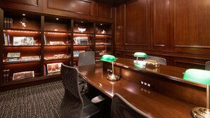 A conference room with a long wooden table, two chairs, a desk lamp, and a bookshelf filled with books and decorative items. - GRG Hotel Naha (Naha)