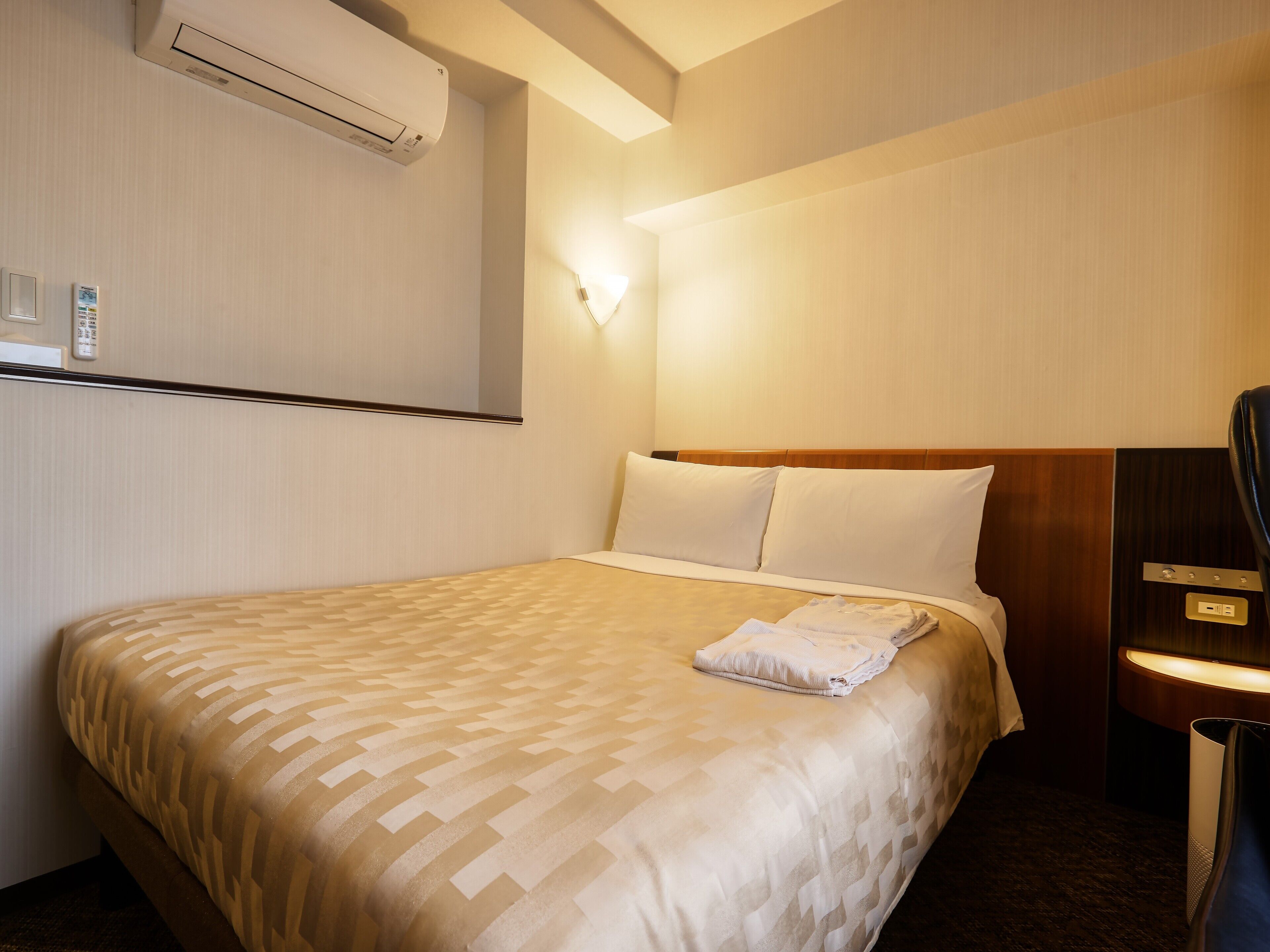 Une chambre d’hôtel équipée d’un lit, d’une table de chevet, d’un climatiseur et d’une lampe fixée au mur.