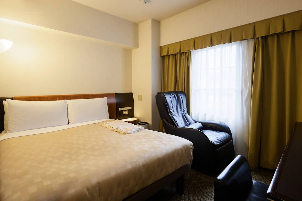 A hotel room with a large bed, a desk, a chair, and a window with curtains.
