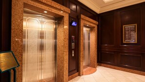 A hotel lobby with two elevators, a marble floor, and a wall-mounted information board. - GRG Hotel Naha (Naha)