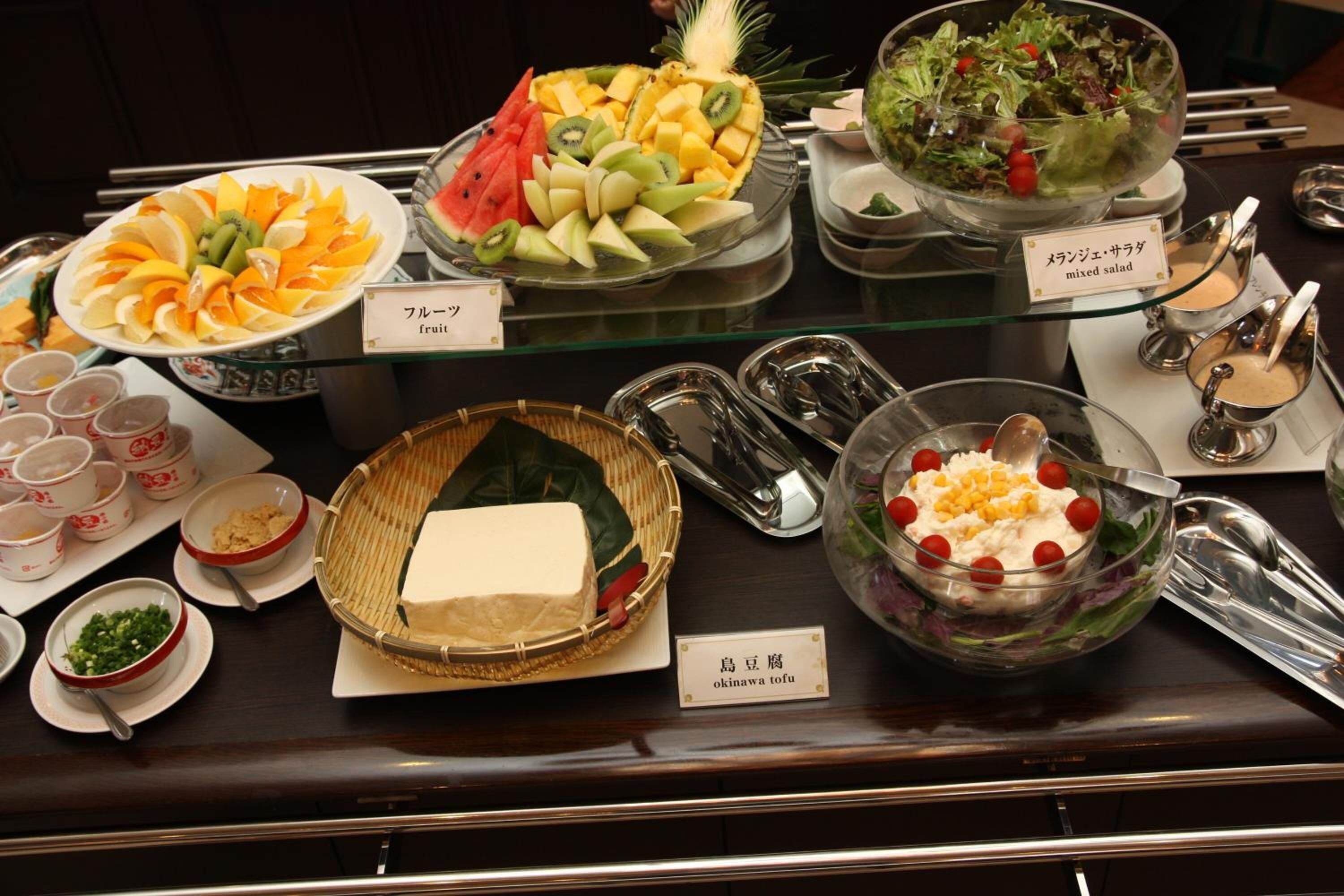 Un bufé con diversos platos, entre ellos fruta, ensalada y tofu.