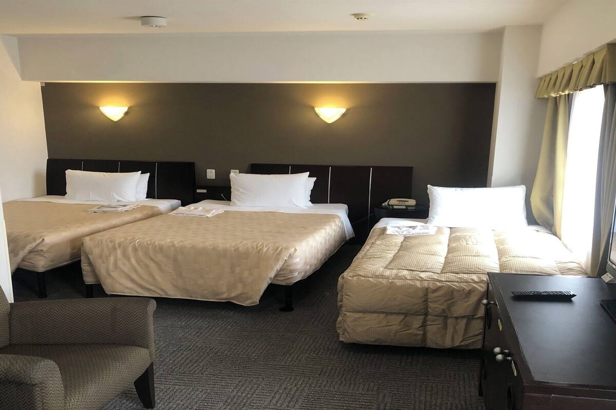 A hotel room with two beds, a sofa, a TV, and a desk.