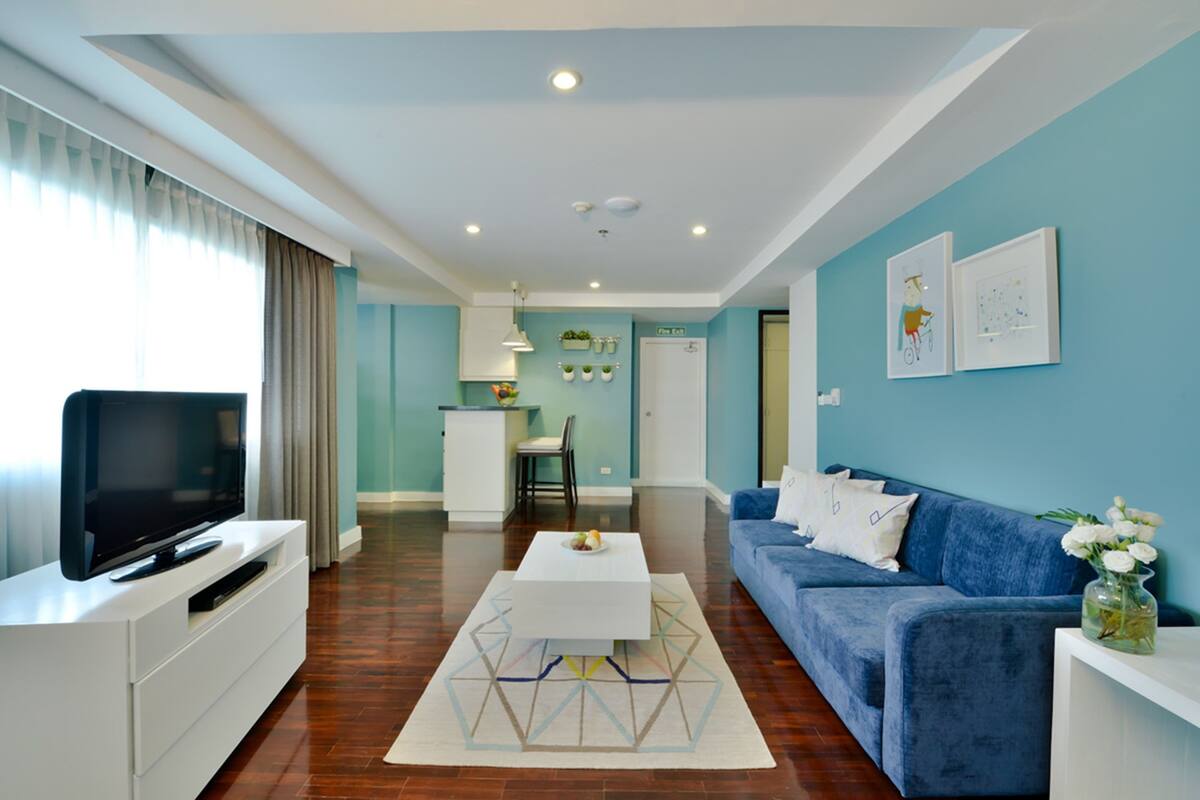 A modern living room with a flat-screen TV, a blue sofa, and a dining area with a white table and chairs.