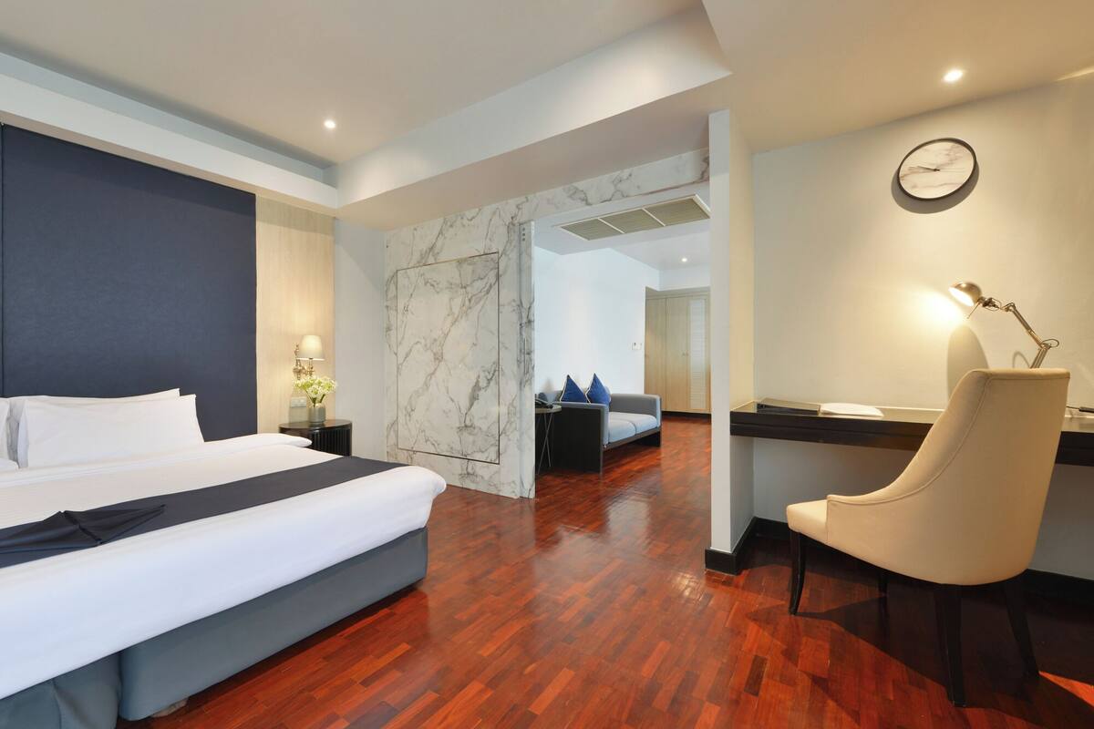 A hotel room with a bed, desk, chair, and a clock on the wall.
