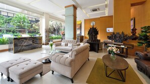 Un hall d’hôtel moderne comprenant un comptoir d’accueil, un espace salon et une grande fenêtre donnant sur un jardin.