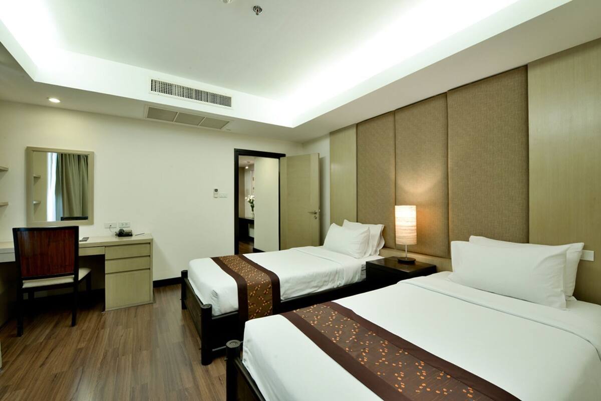 A hotel room with two beds, a desk, a chair, a mirror, and a nightstand with a lamp.