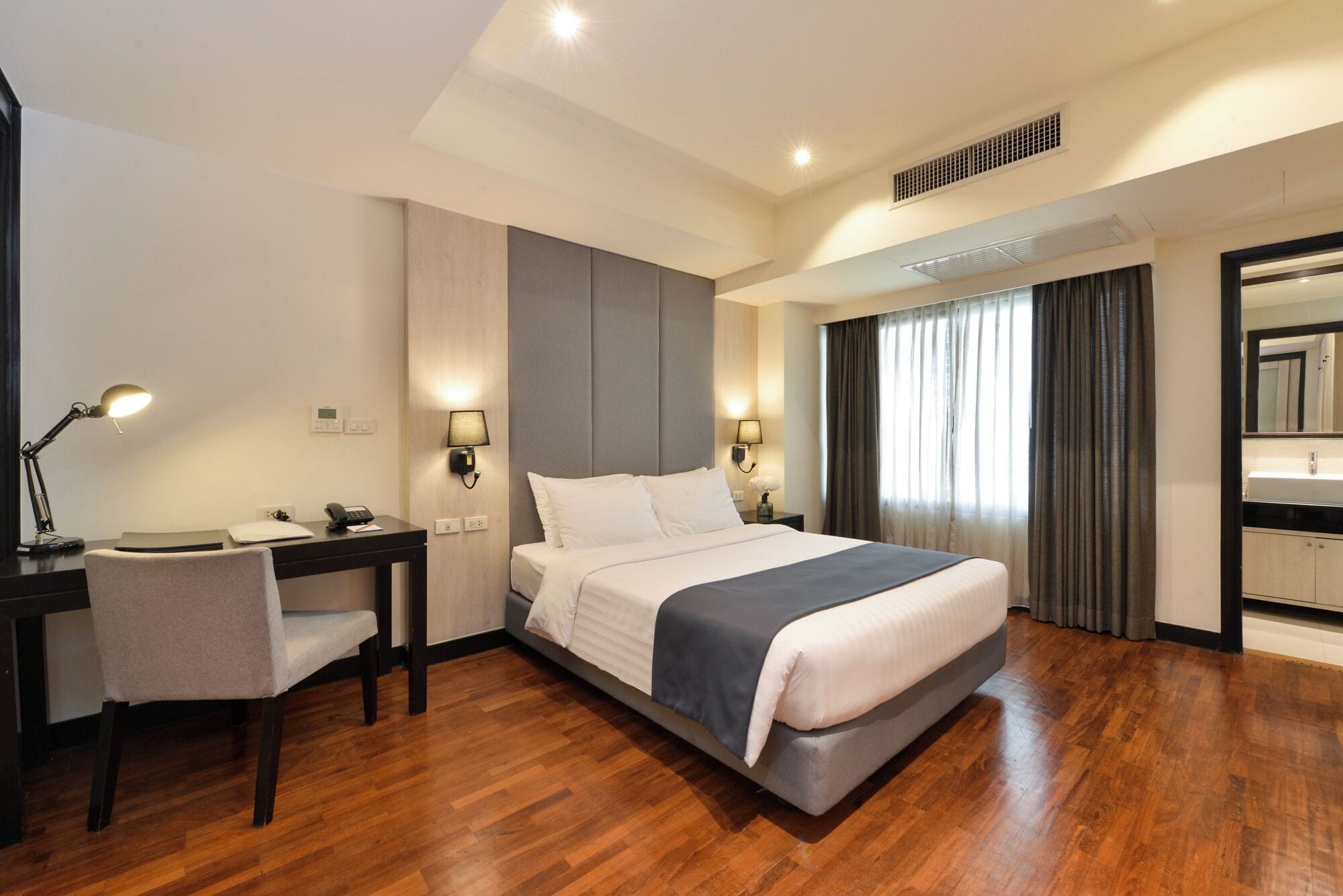 Una habitación de hotel con cama, escritorio, silla y baño con espejo y lavabo.