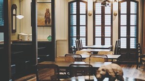 Un coin repas avec une table et des chaises en bois, un lustre et de grandes fenêtres équipées de volets.