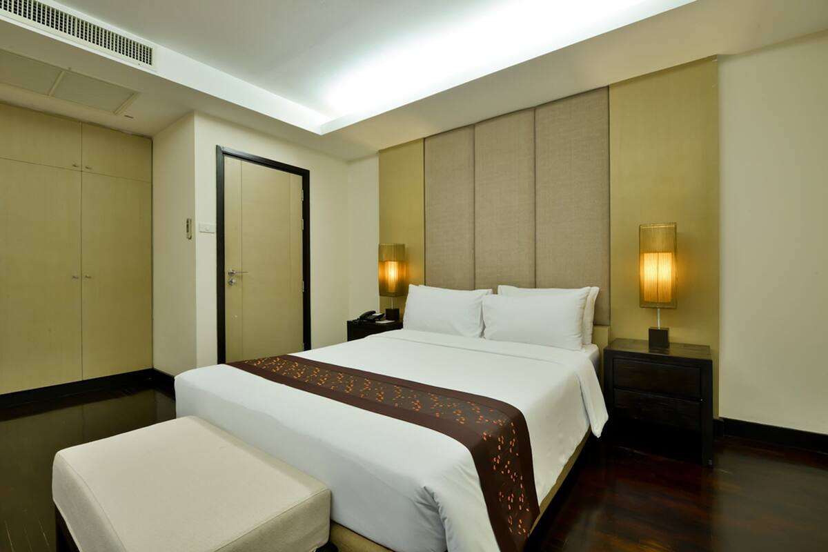 A hotel room with a large bed, bedside tables, a wardrobe, and a bench.