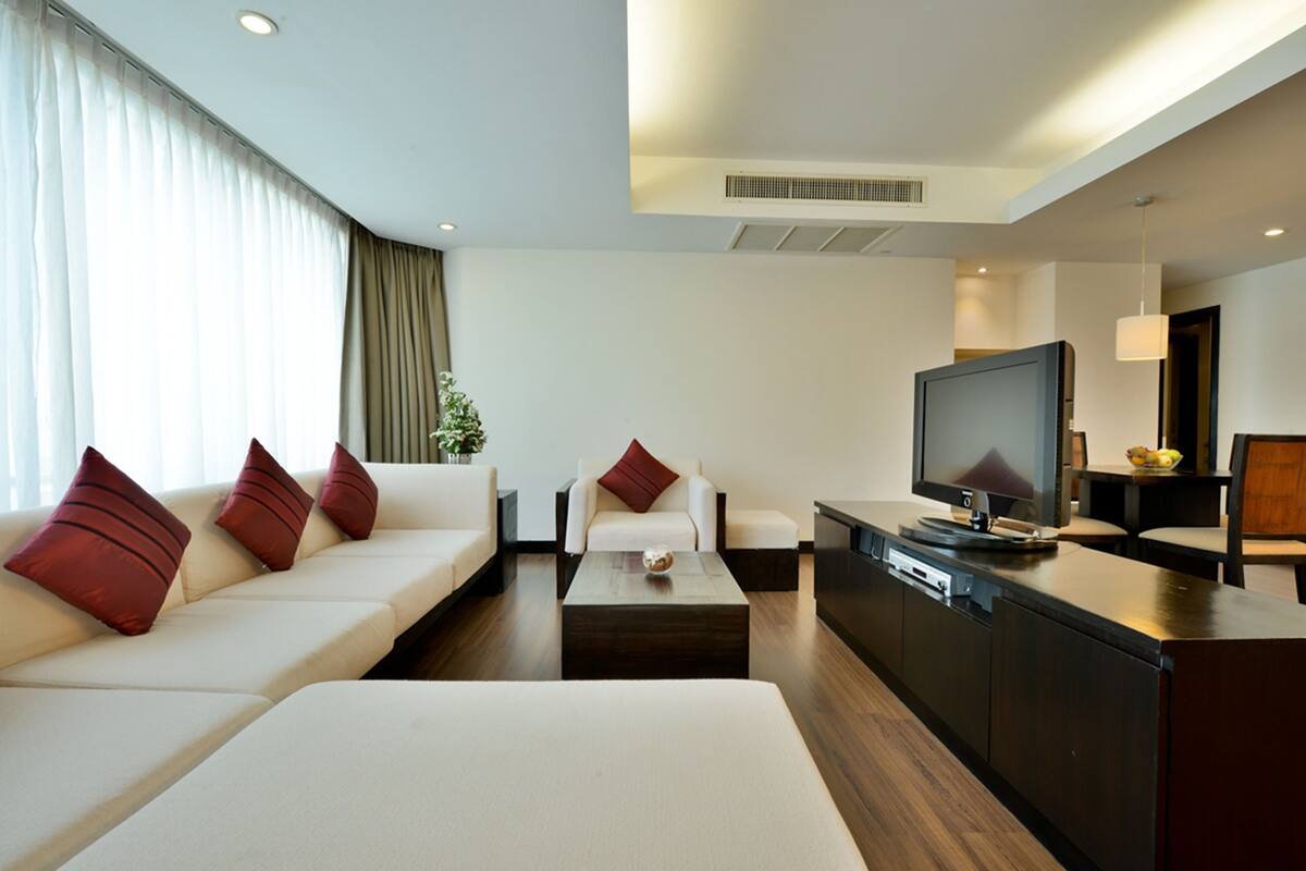 A modern hotel room with a sofa, a coffee table, a TV, and a dining area.