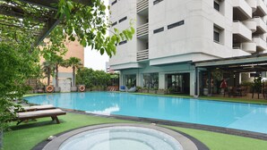 Une piscine avec un jacuzzi, entourée d’une pelouse et d’un bâtiment doté de balcons.