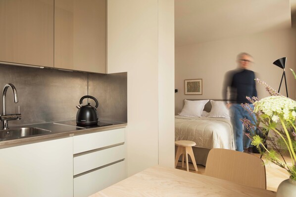 A modern kitchen with stainless steel appliances, a wooden dining table, and a minimalist bedroom with a bed and bedside table. - Grand Hôtel Richer (Paris)