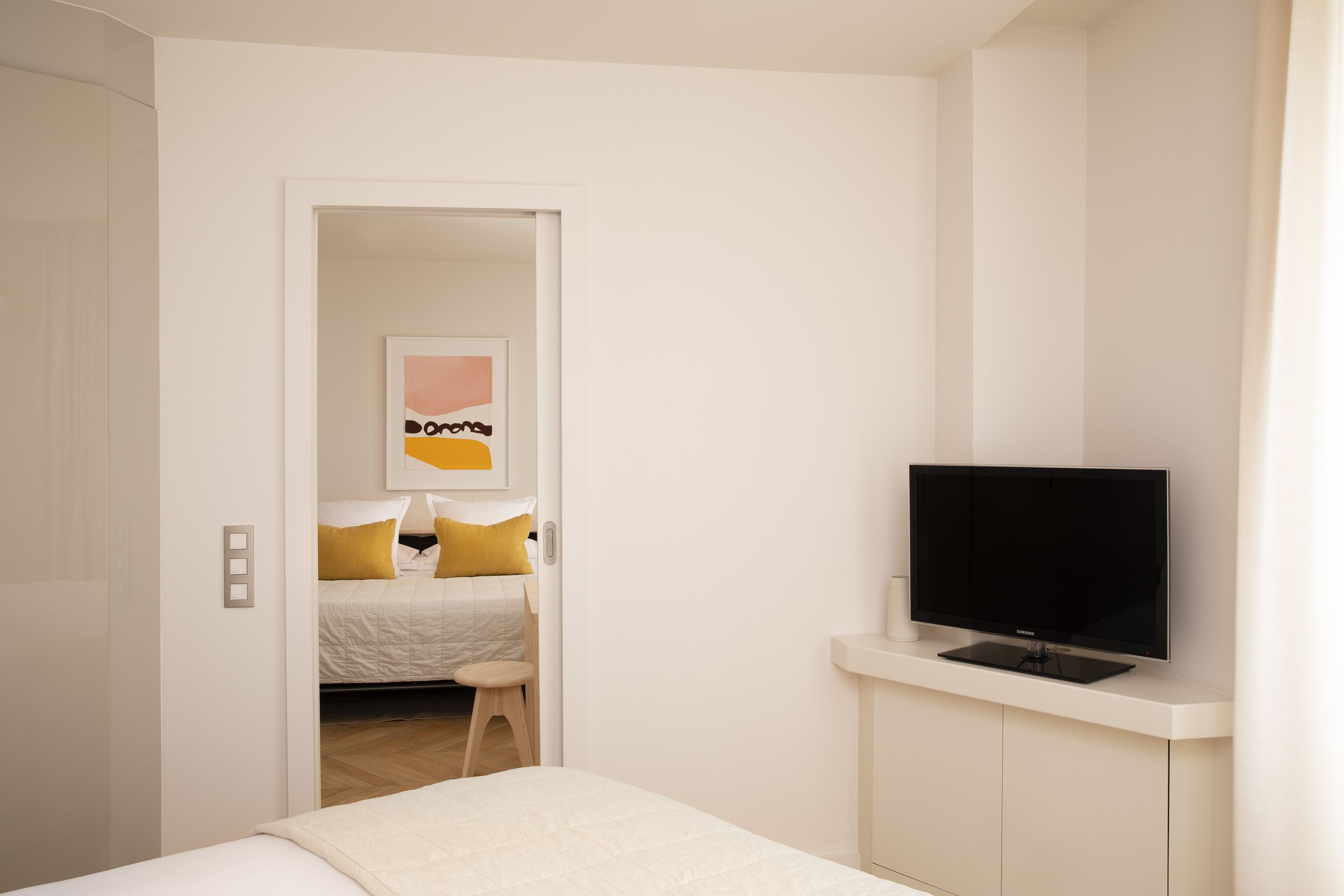 Ein modernes Hotelzimmer mit einem Bett, einem Fernseher auf einem Schrank und einer Tür zu einem weiteren Raum.