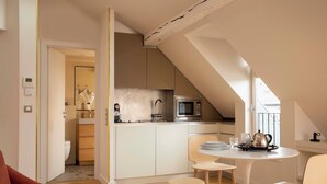 A modern kitchen with a microwave, sink, and cabinets, a dining area with a table and chairs, and a visible bathroom with a toilet. - Grand Hôtel Richer (Paris)