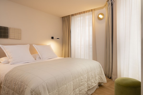 A neatly made bed with a white duvet, a green ottoman, and a wall-mounted light fixture. - Grand Hôtel Richer (Paris)