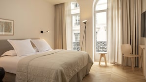 A bedroom with a bed, a chair, a desk, a floor lamp, and a window with curtains. - Grand Hôtel Richer (Paris)