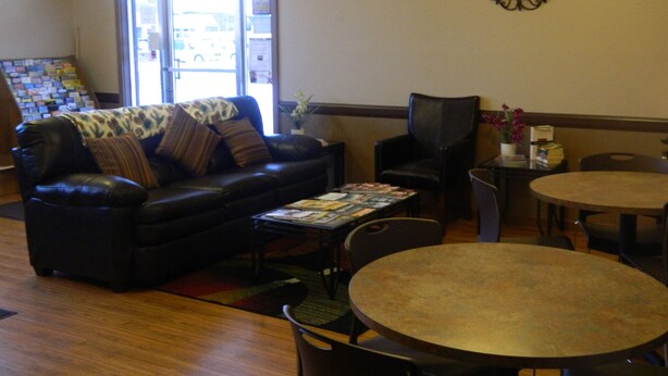 A living room with a black leather sofa, a coffee table, a round table, and a chair. There is a door with a view of the outside. - Country Motor Inn (Livingston)